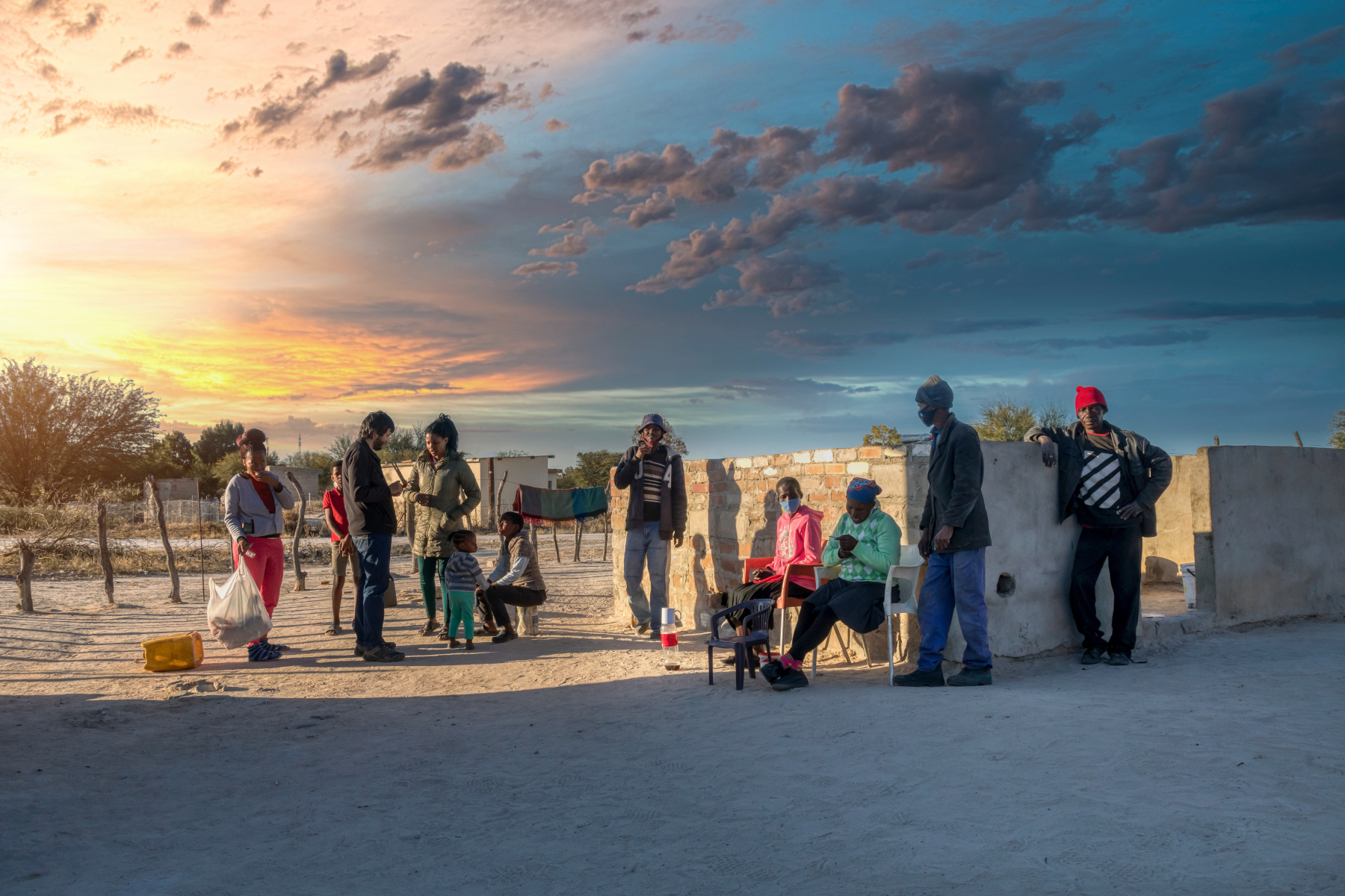 Extended African family talking with a Caucasian man in the yard of a house in a village in Botswana